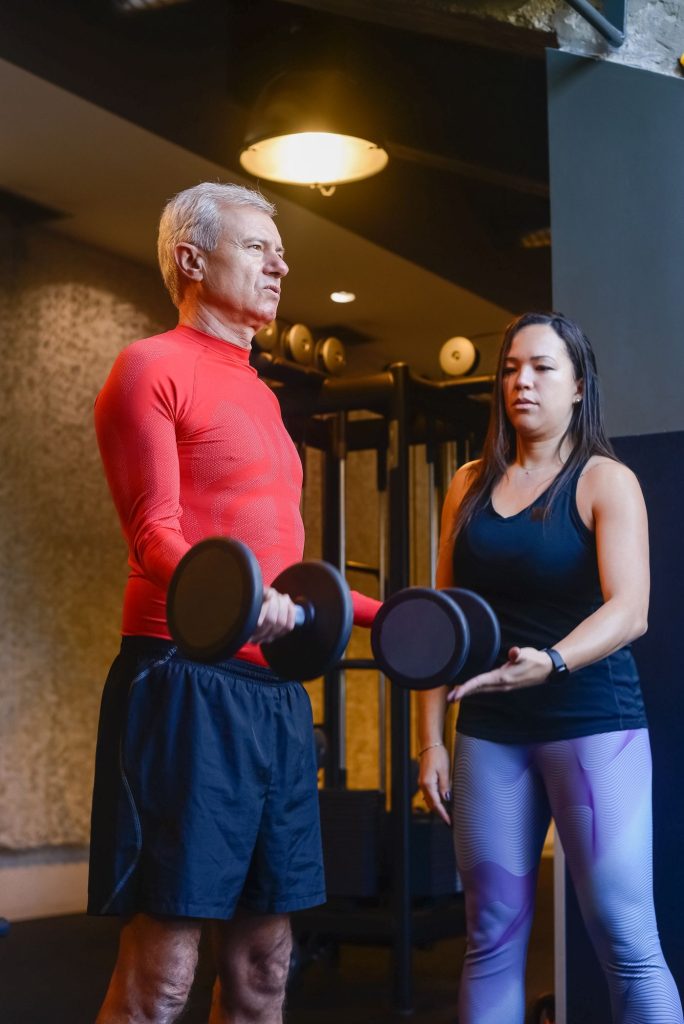 Personal trainer guiding an older adult through a dumbbell exercise during a supervised strength session